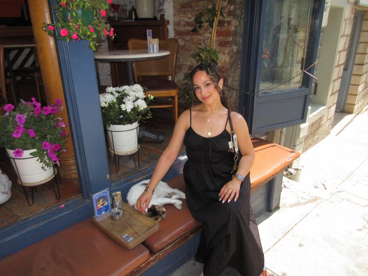 Bushra Alimerdan smiling, sitting on a bench, and petting a cat that is curled up alongside.